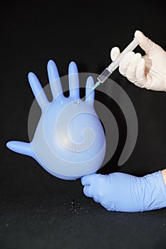Inflated blue glove and gloved hand injecting a liquid with a syringe
