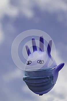 Inflated medical glove with a medical mask on against the blue sky.