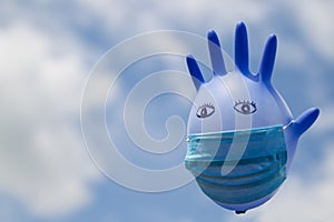 Inflated medical glove with a medical mask on against the blue sky.