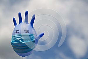 Inflated medical glove with a medical mask on against the blue sky.