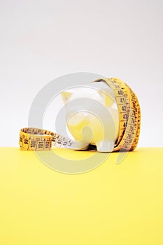 Inflation concept - White Piggy Bank wrapped up in a measuring tape on a yellow surface