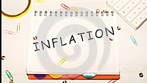 Inflation word on a checkered notebook on a light table next to a magnifying glass, paper clips, stationery buttons, a calculator