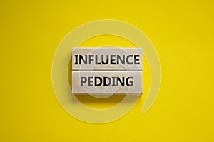 Influence pedding symbol. Wooden blocks with words `Influence pedding` on beautiful yellow background. Business and Influence