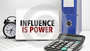 influence is power words on white notebook and calculator, black vintage alarm clock and blue paper folder