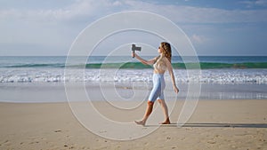 Influencer in white outfit records beach vlog with pro camera, wireless lav mic. Travel blogger captures ocean views