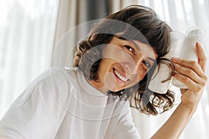 Influential young caucasian girl is looking at camera holding jars of facial foam indoors.