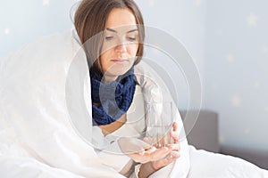 Influenza treatment or coronavirus . Flu-sick woman, wrapped in warm scarf and blanket , taking pills holding glass of water