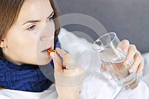Influenza treatment or coronavirus . Flu-sick woman, wrapped in warm scarf and blanket , taking pills holding glass of water