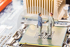 Information Technology security or IT success concept. Two miniature businessmen IT managers shaking hands while standing on CPU a