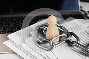 Information warfare concept. Chained wooden figure, laptop and newspapers on table, closeup