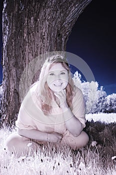 Infrared Photo of a Girl sitting under a Tree under a blue Sky