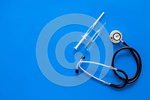 Infuenza, flu vaccine in syringe near stethoscope on blue background top view copy space