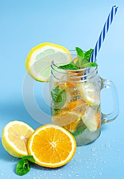 Infused detox water with ice, lemon and oranges slices with mint on blue background. Iced cold summer cocktail or lemonade in