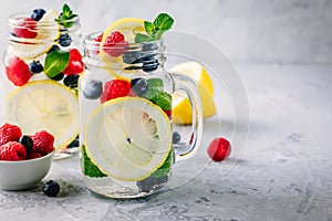 Infused detox water with lemon slice, raspberry, blueberry and mint. Ice cold summer cocktail or lemonade in mason jar