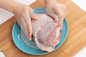 Ingredient for a healthy broth. Female hands rub the raw leg of turkey with spices