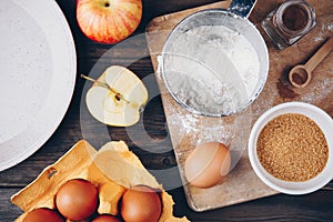 Ingredients for apple pie cooking with fresh red apples, flour, eggs, brown sugar and spices