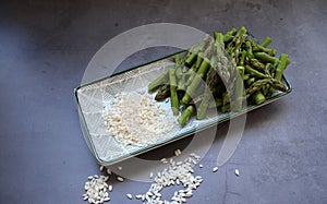 ingredients for asparagus risotto, plate with sliced green asparagus, arborio rice,