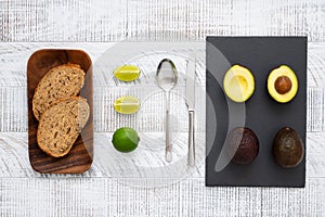 Ingredients for avocado toast. Slices  of fresh rye bread, lime, avocados, spoon and knife on the white wooden table. Healthy nutr