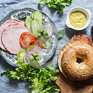 Ingredients for the bagel sandwich with ham, vegetables and green salad on a blue background, top view