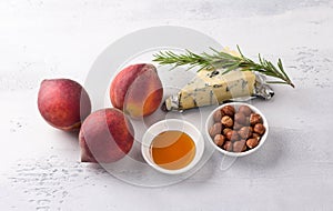 Ingredients for baked peaches: fresh peaches, blue cheese, hazelnuts, honey and rosemary on a light gray background