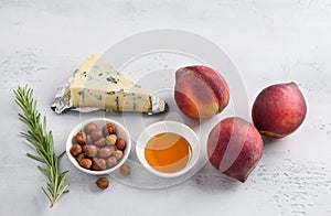 Ingredients for baked peaches: fresh peaches, blue cheese, hazelnuts, honey and rosemary on a light gray background