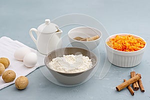 Ingredients for baking carrot cake. Flour, grated carrots, eggs, milk, walnuts, spices are located on the kitchen table in gray.