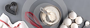 Ingredients for baking on a dark gray background: flour, eggs, baking powder, heart shape, whisk, textiles. top view. Layout of a