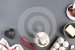 Ingredients for baking on a dark gray background: flour, eggs, butter, heart shape, whisk, textiles. top view. Layout of
