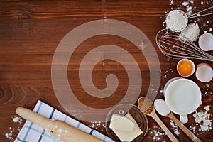 Ingredients for baking dough including flour, eggs, milk, butter, sugar, whisk and rolling pin on wooden rustic background