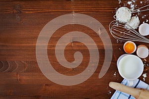 Ingredients for baking dough including flour, eggs, milk, whisk and rolling pin on wooden rustic background photo