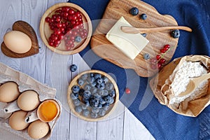 Ingredients for baking lie on a light wooden background with a blue kitchen towel. butter, berries and wooden