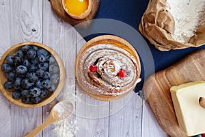 Ingredients for baking lie on a light wooden background with a blue kitchen towel. flour, eggs, butter, berries and wooden