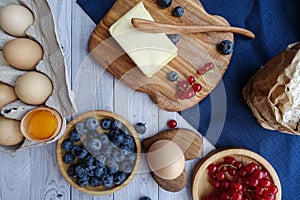 Ingredients for baking lie on a light wooden background with a blue kitchen towel. flour, eggs, butter, berries and wooden