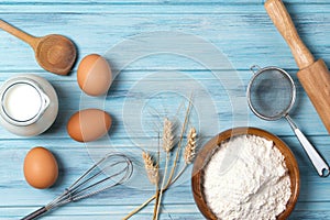 Ingredients for baking, milk, eggs, wheat flour and kitchenware on blue wooden background, top view