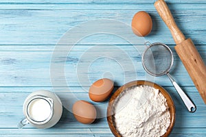 Ingredients for baking, milk, eggs, wheat flour and kitchenware on blue wooden background, top view