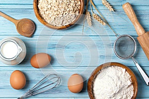 Ingredients for baking, milk, eggs, wheat flour, oats and kitchenware on blue wooden background, top view