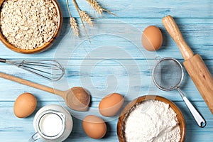 Ingredients for baking, milk, eggs, wheat flour, oats and kitchenware on blue wooden background, top view