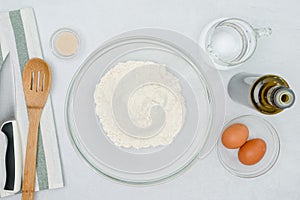 Ingredients for baking needs close up on light grey background. Flour, yeast, eggs, oil, and warm water