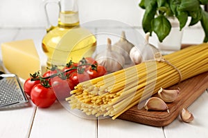 Ingredients for bucatini recipe: pasta, tomatoes, oil, basil, garlic, cheese on white wooden background.