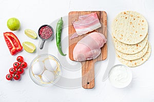 Ingredients for chicken tacos, , tomatoes, corn, egg, pepper,lime chicken meat and tortillas over white textured background top