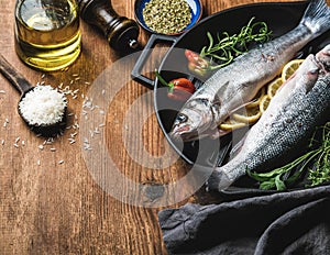 Ingredients for cookig healthy fish dinner. Raw uncooked seabass with rice, olive oil, lemon slices, herbs and spices