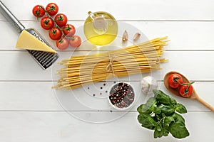 Ingredients for cooking bucatini with tomatoes, basil, cheese and garlic on white wooden background.