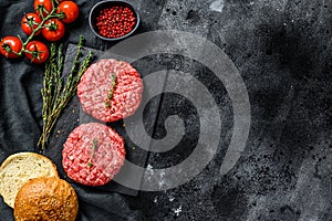 Ingredients for cooking burgers. Minced beef patties, buns, tomatoes, herbs and spices. Black background. Top view. Copy