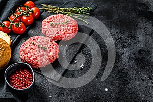 Ingredients for cooking burgers. Minced beef patties, buns, tomatoes, herbs and spices. Black background. Top view. Copy space photo