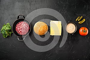 Ingredients for cooking burgers. Minced beef patties, buns, tomatoes, herbs and spices, on black stone background, top view flat