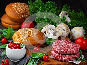 Ingredients for cooking burgers. Raw ground beef meat cutlets on wooden chopping board, onion, cherry tomatoes, greens, tomato