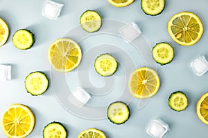 Ingredients for cooking cold spring lemonade drink with cucumber, pieces of lemon, ice cubes on blue background, top view