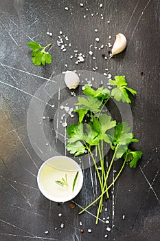 Ingredients for cooking on a dark stone table - parsley, olive oil, garlic and spices.