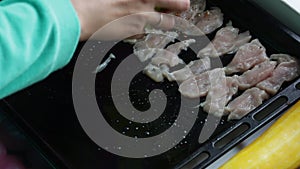 Ingredients for cooking dinner. The woman puts pieces of chicken fillet on a baking sheet and sprinkles with spices.