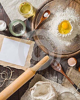 Ingredients for cooking dough or bread. Broken egg on top of a bunch of white rye flour. Dark wooden background.